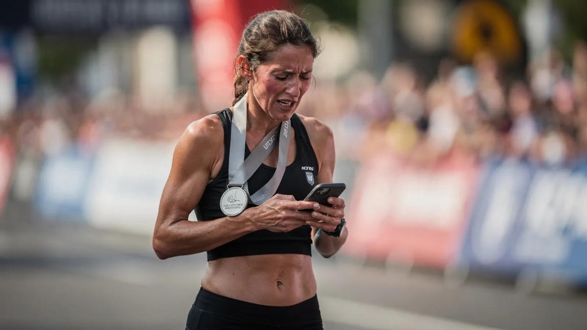 Coureuse avec sa médaille de finisher regardant son téléphone juste après la ligne d'arrivée d'un marathon